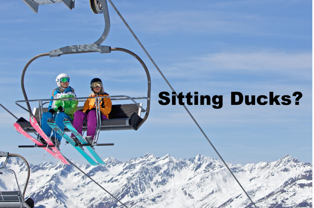 Image of two colorfully dressed skiers on a chairlift with a beautiful panoramic view of mountains in the background.